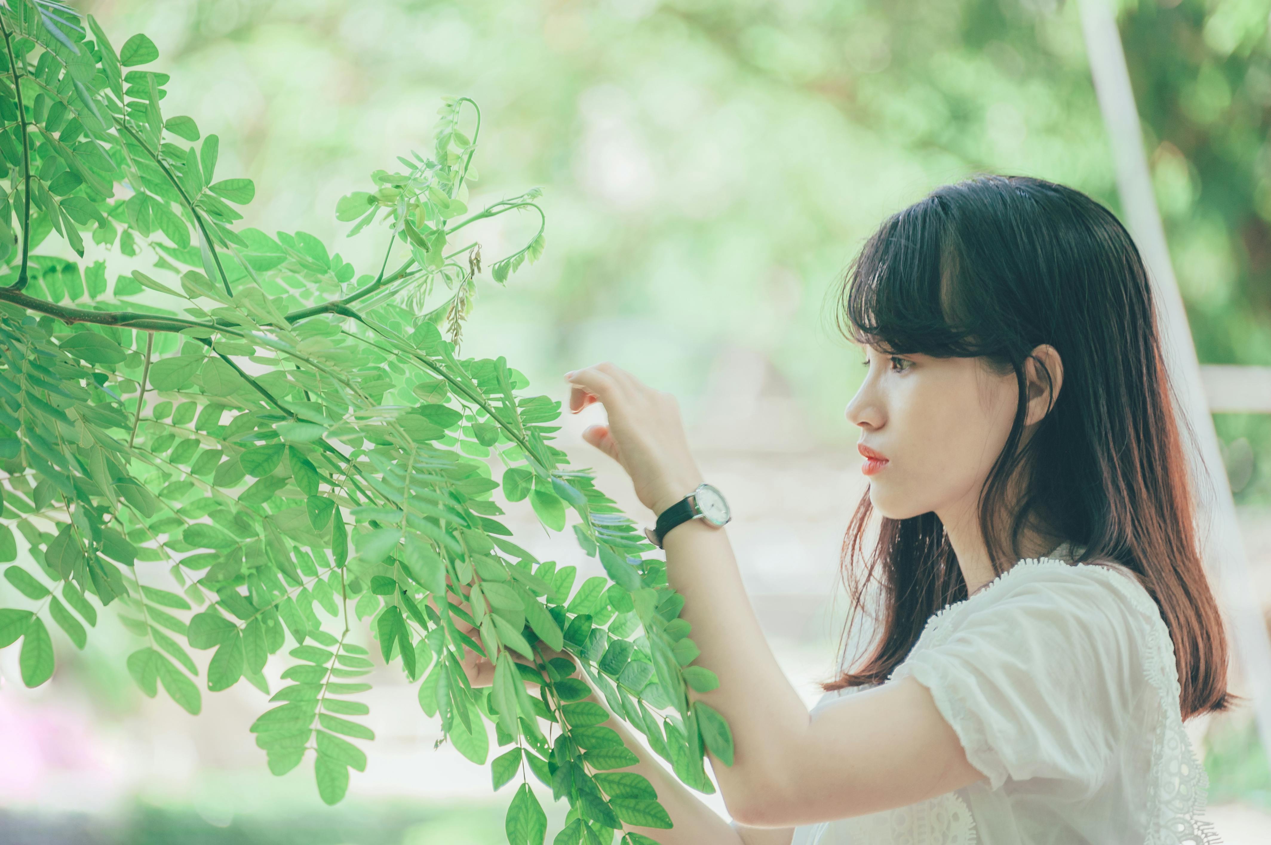 A serene portrait of a young woman interacting with leaves in a lush outdoor setting.